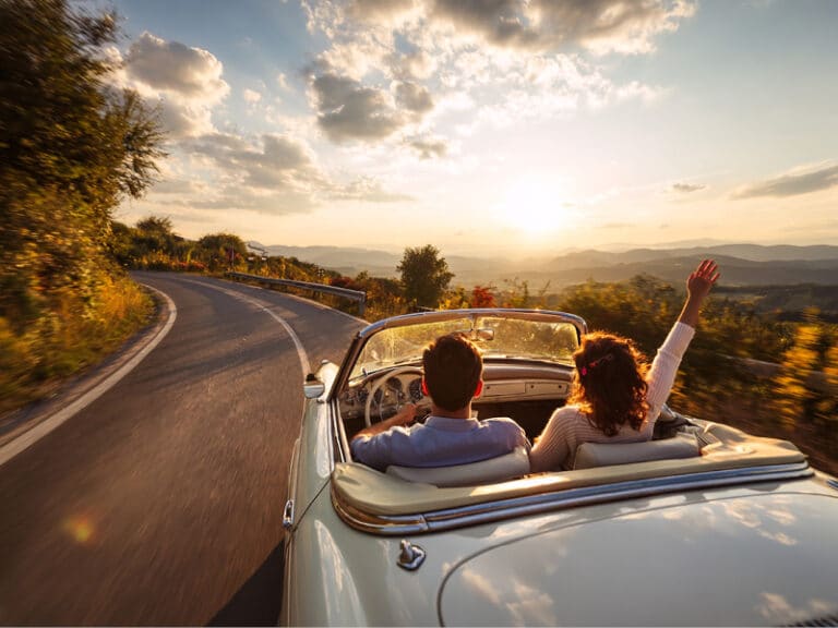 Mann und Frau fahren im Cabrio in schöner Landschaft der Sonne entgegen