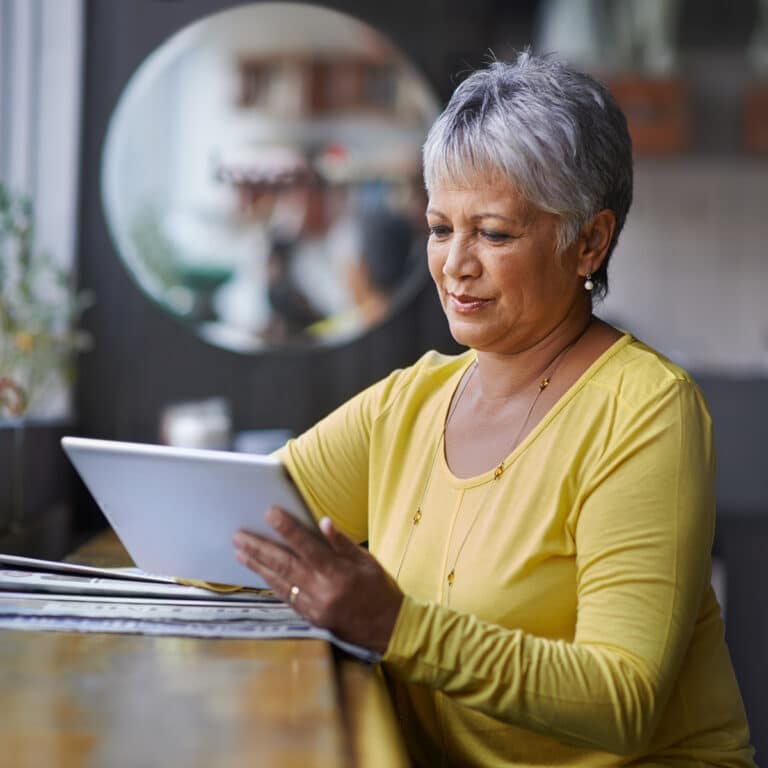 Frau sitzend am Tisch mit Tablet und Zeitung