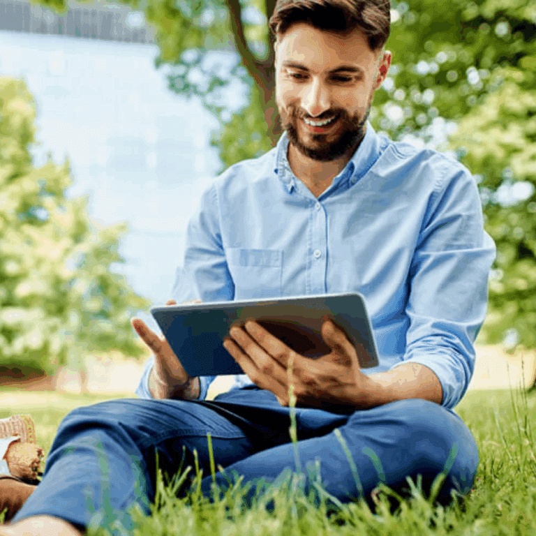 Mann sitzend auf Wiese mit Tablet in der Hand